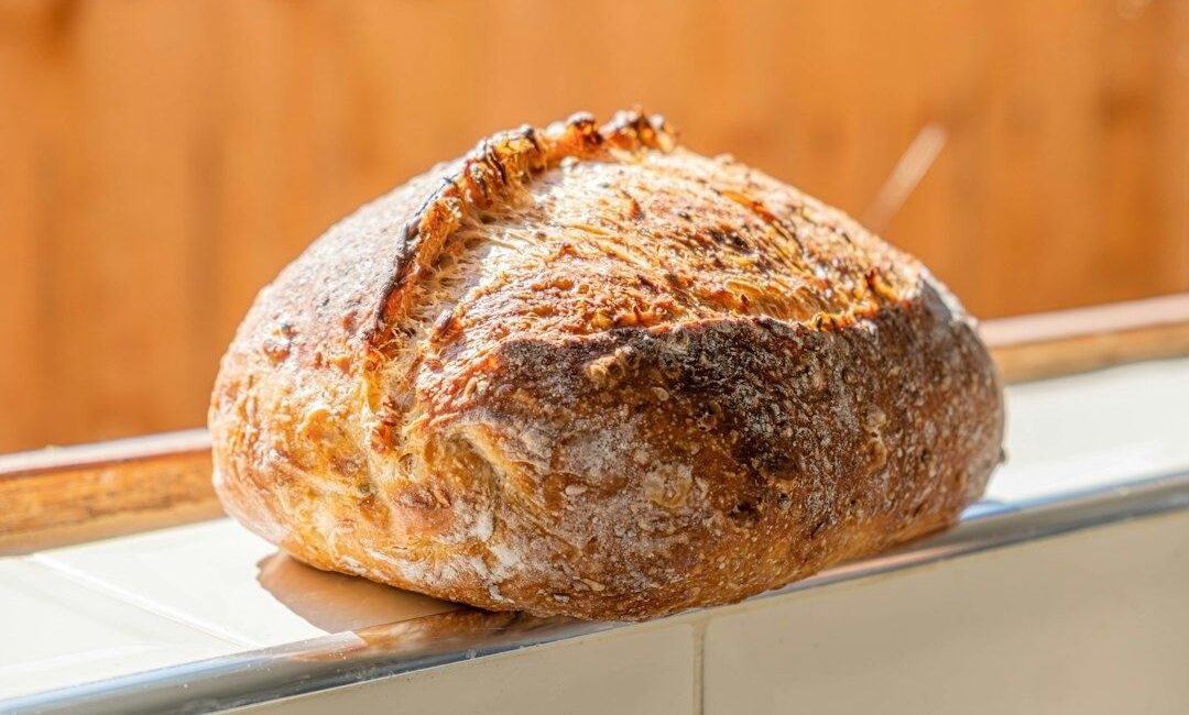 Runt, gyllenbrunt bröd med mjölad, sprucken skorpa på en bänk